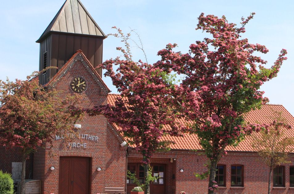 Kirche mit rotem Klinkerstein, davor Bäume mit rosa Blüten
