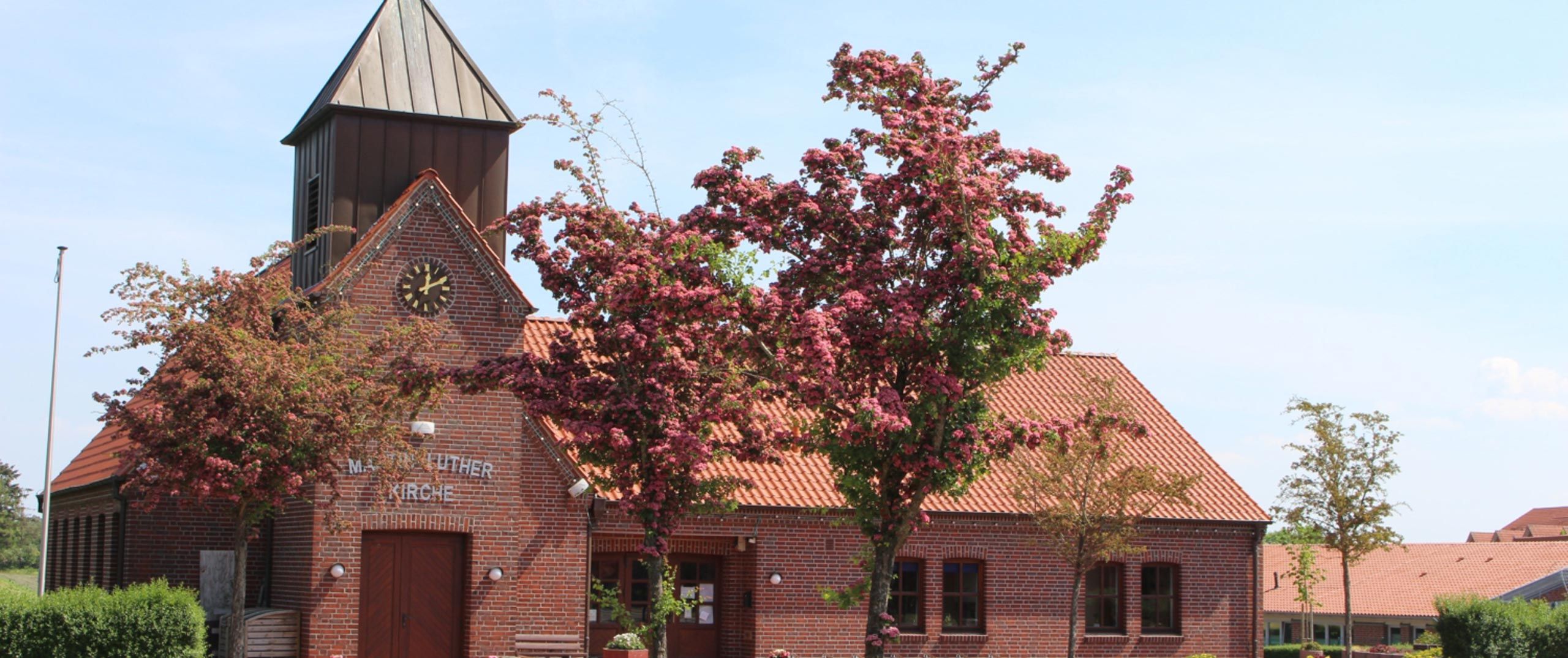 Kirche mit rotem Klinkerstein, davor Bäume mit rosa Blüten